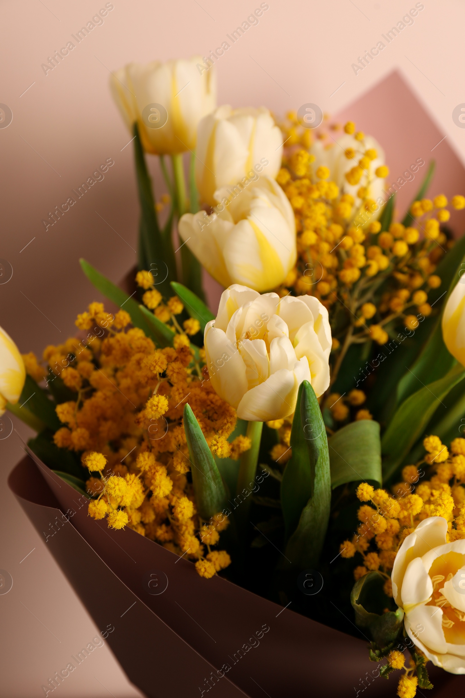Photo of Bouquet of beautiful spring flowers near beige wall, closeup