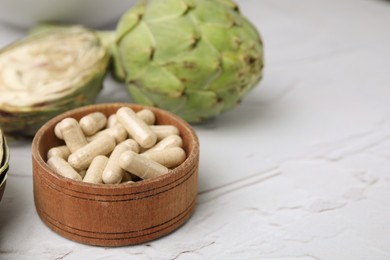 Bowl with pills and fresh artichokes on white textured table, closeup. Space for text