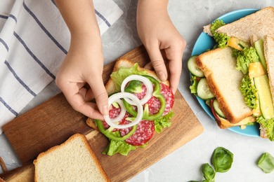 Photo of Woman adding onion to tasty sandwich at light grey marble table, top view