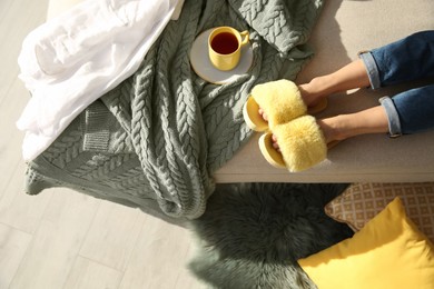 Photo of Woman with cup of tea wearing soft comfortable slippers at home, top view