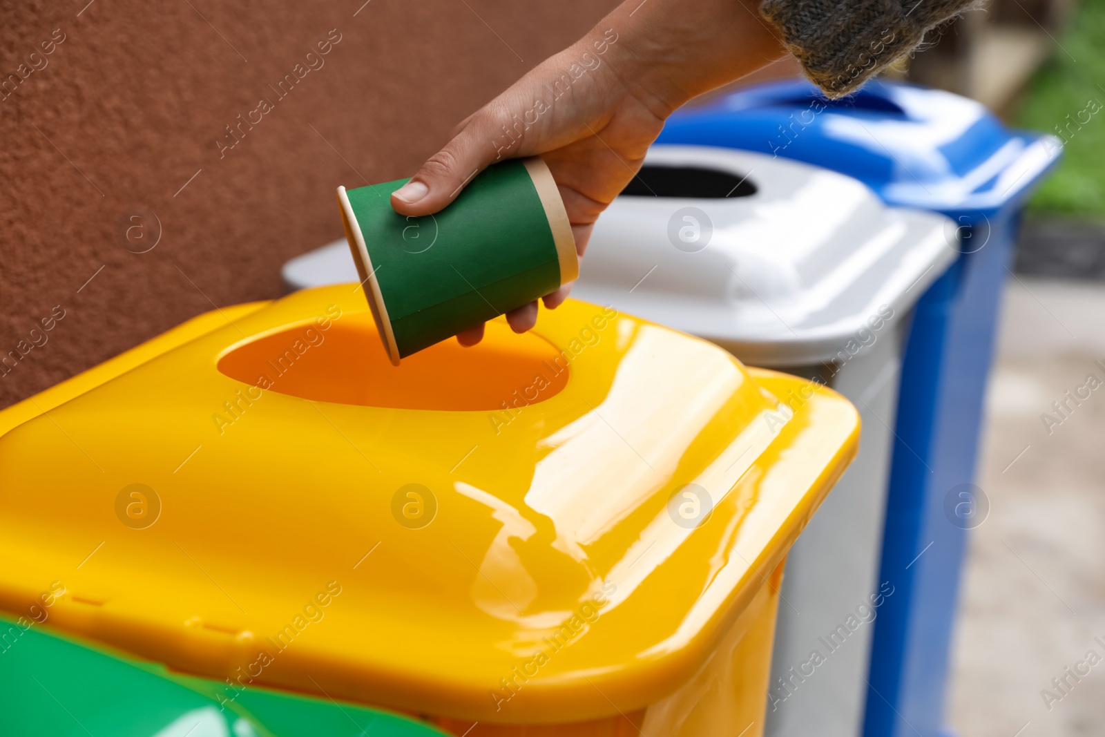 Photo of Woman throwing coffee cup into recycling bin outdoors, closeup