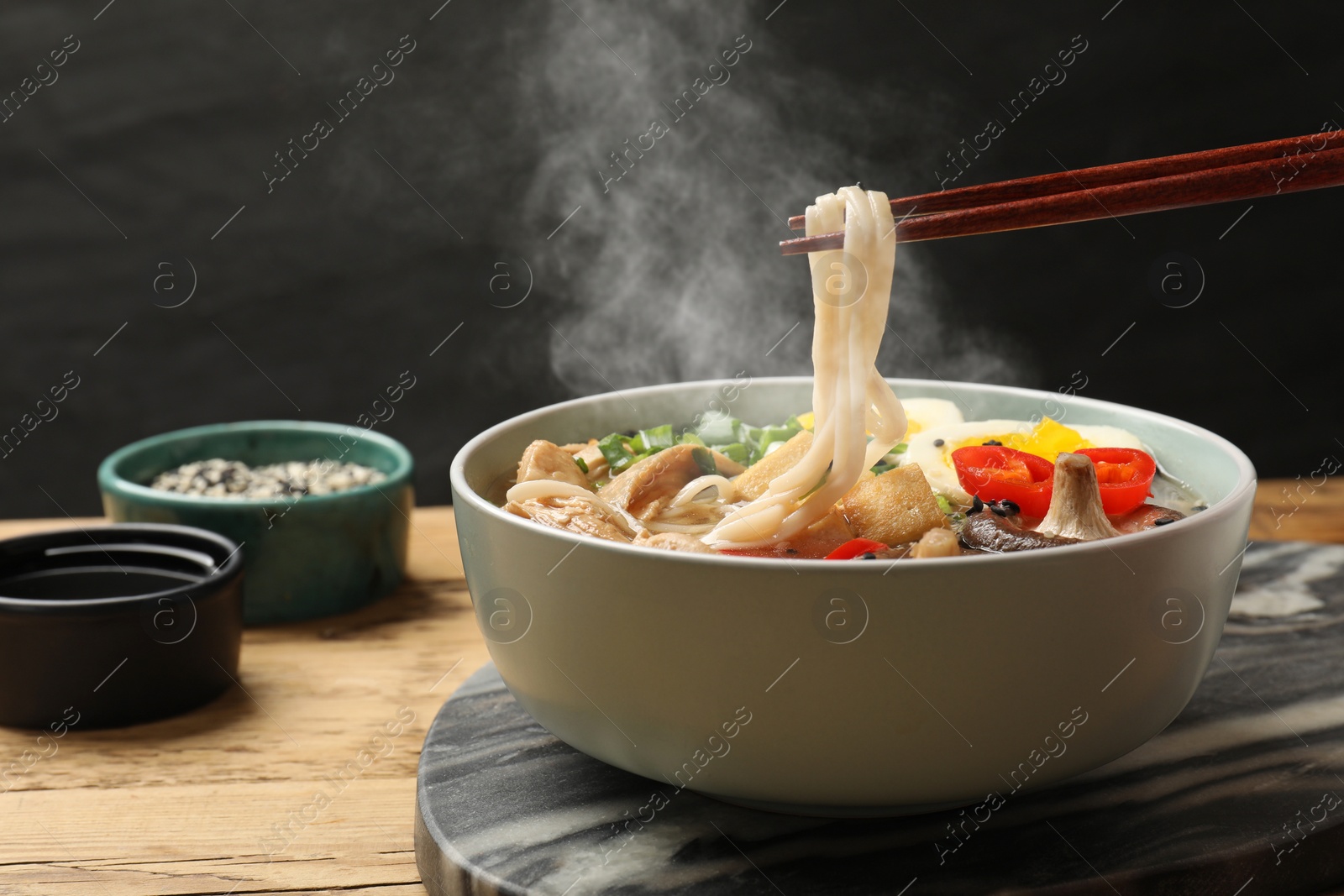 Image of Eating hot ramen with chopsticks at wooden table, closeup. Noodle soup