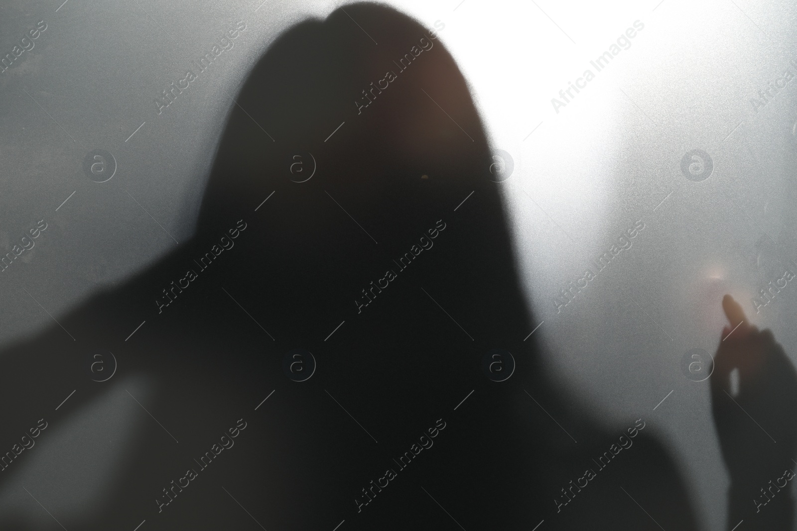 Photo of Silhouette of ghost behind glass against light grey background