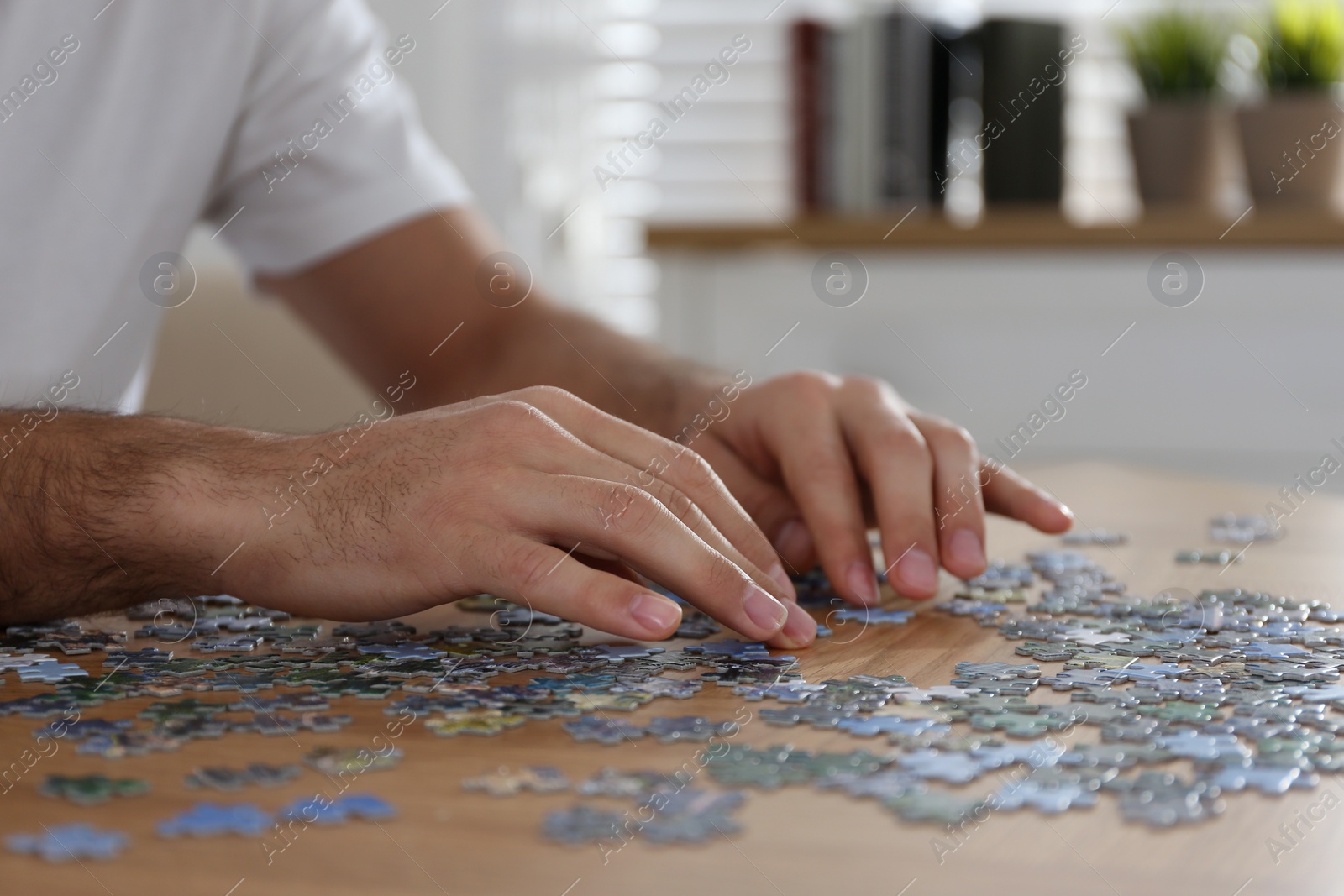 Photo of Man playing with puzzles at wooden table indoors, closeup