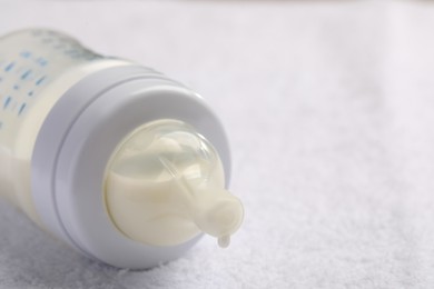 Photo of Feeding bottle with baby formula on white soft towel, closeup. Space for text