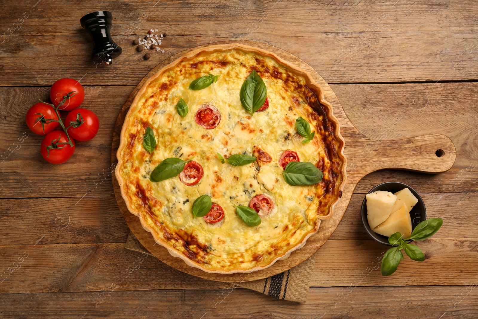 Photo of Delicious quiche with cheese, tomatoes and basil on wooden table, flat lay