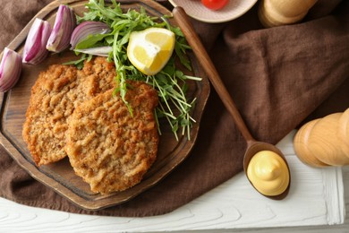 Photo of Tasty schnitzels served with onion, lemon and microgreens on white wooden table, flat lay