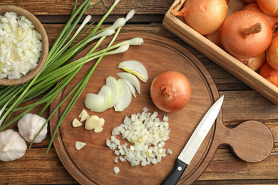 Board with cut onion and garlic on wooden table, flat lay