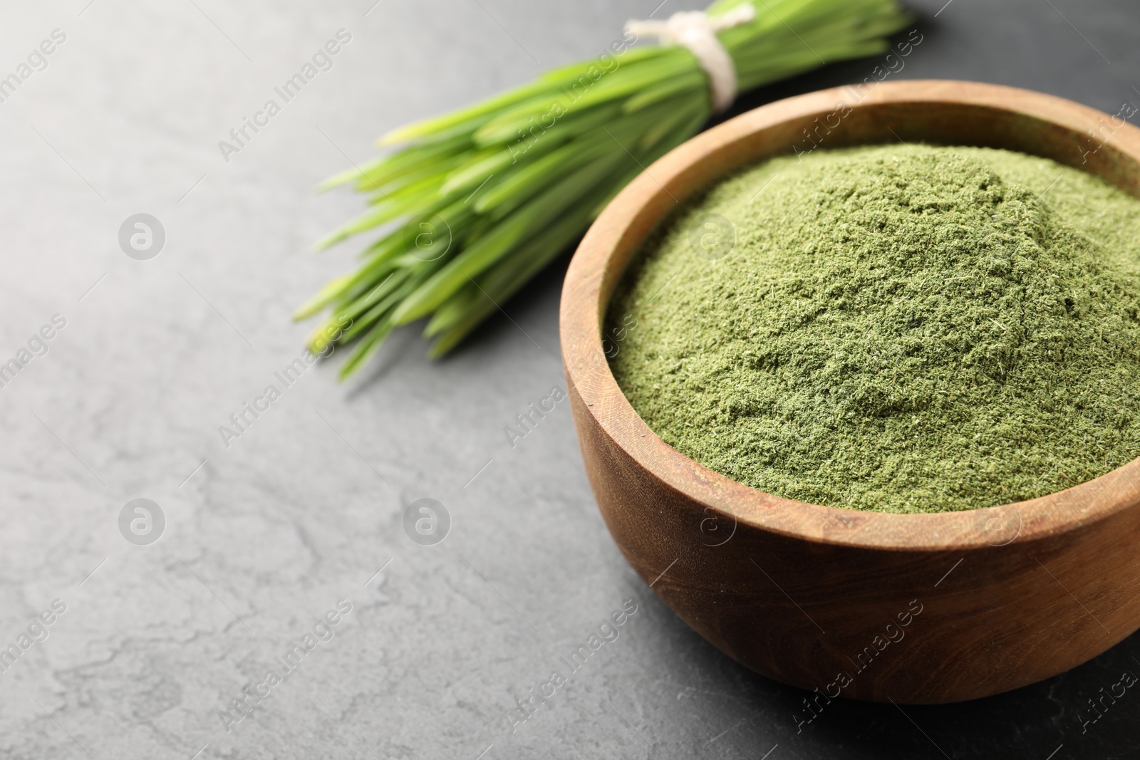 Photo of Wheat grass powder in bowl on grey table, closeup. Space for text