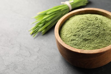 Photo of Wheat grass powder in bowl on grey table, closeup. Space for text