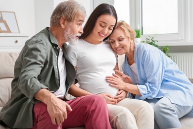 Photo of Happy pregnant woman spending time with her parents at home. Grandparents' reaction to future grandson