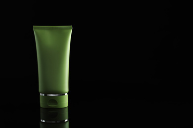 Tube of cosmetic product on black background, space for text