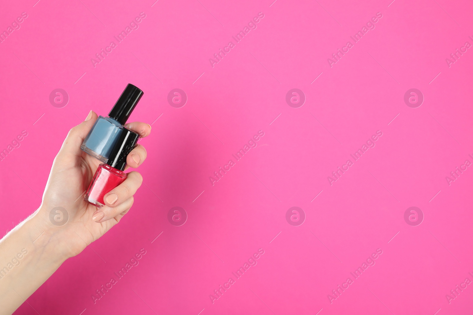 Photo of Woman holding nail polishes on pink background, closeup. Space for text