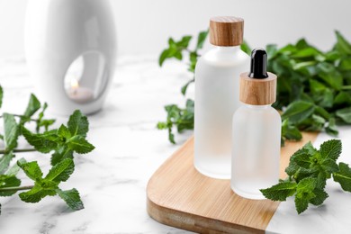 Photo of Bottles of mint essential oil and fresh leaves on white marble table
