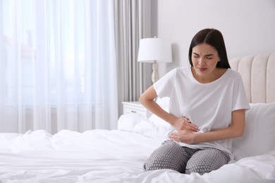 Photo of Young woman suffering from stomach ache in bedroom