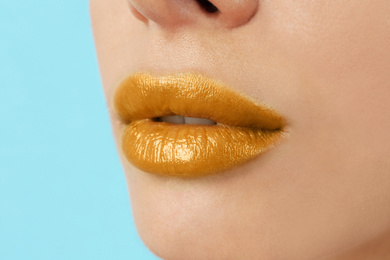 Woman with golden lipstick on light blue background, closeup