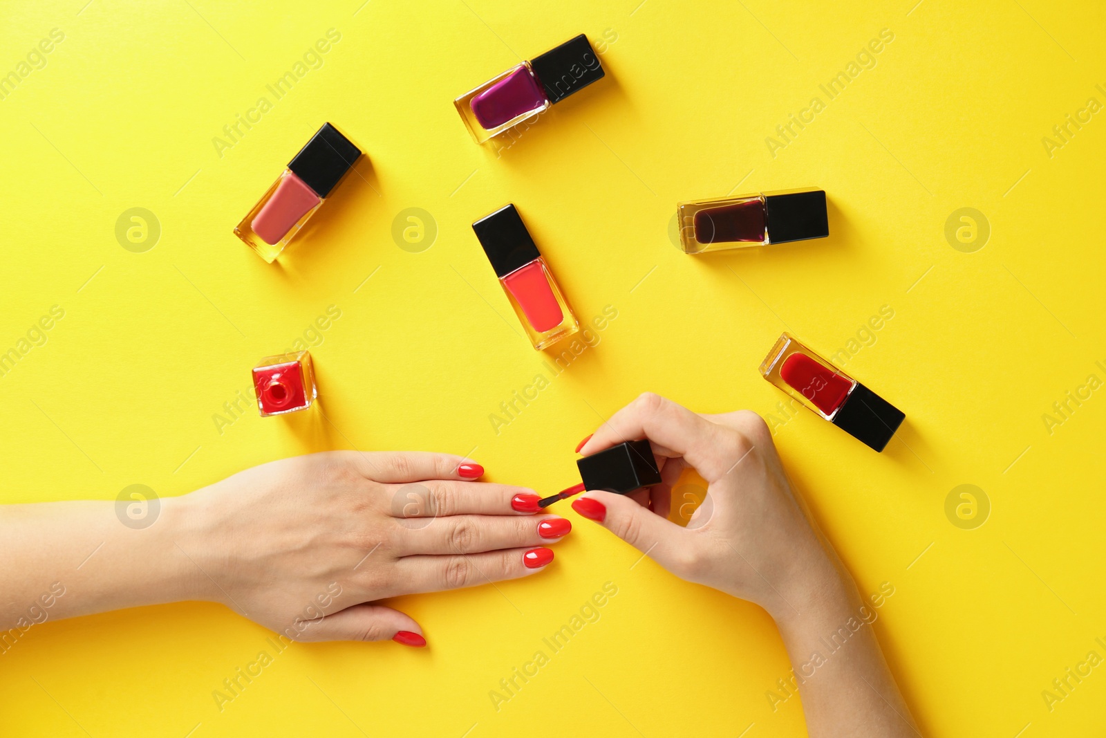 Photo of Woman applying bright nail polish on color background, top view