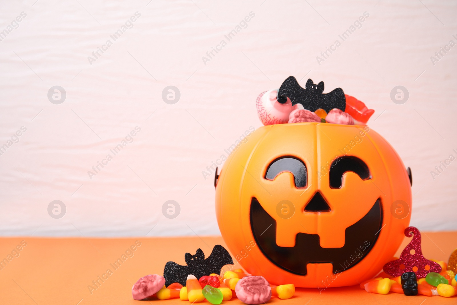 Photo of Halloween trick or treat bucket with different sweets on orange table, space for text