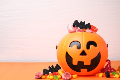 Halloween trick or treat bucket with different sweets on orange table, space for text