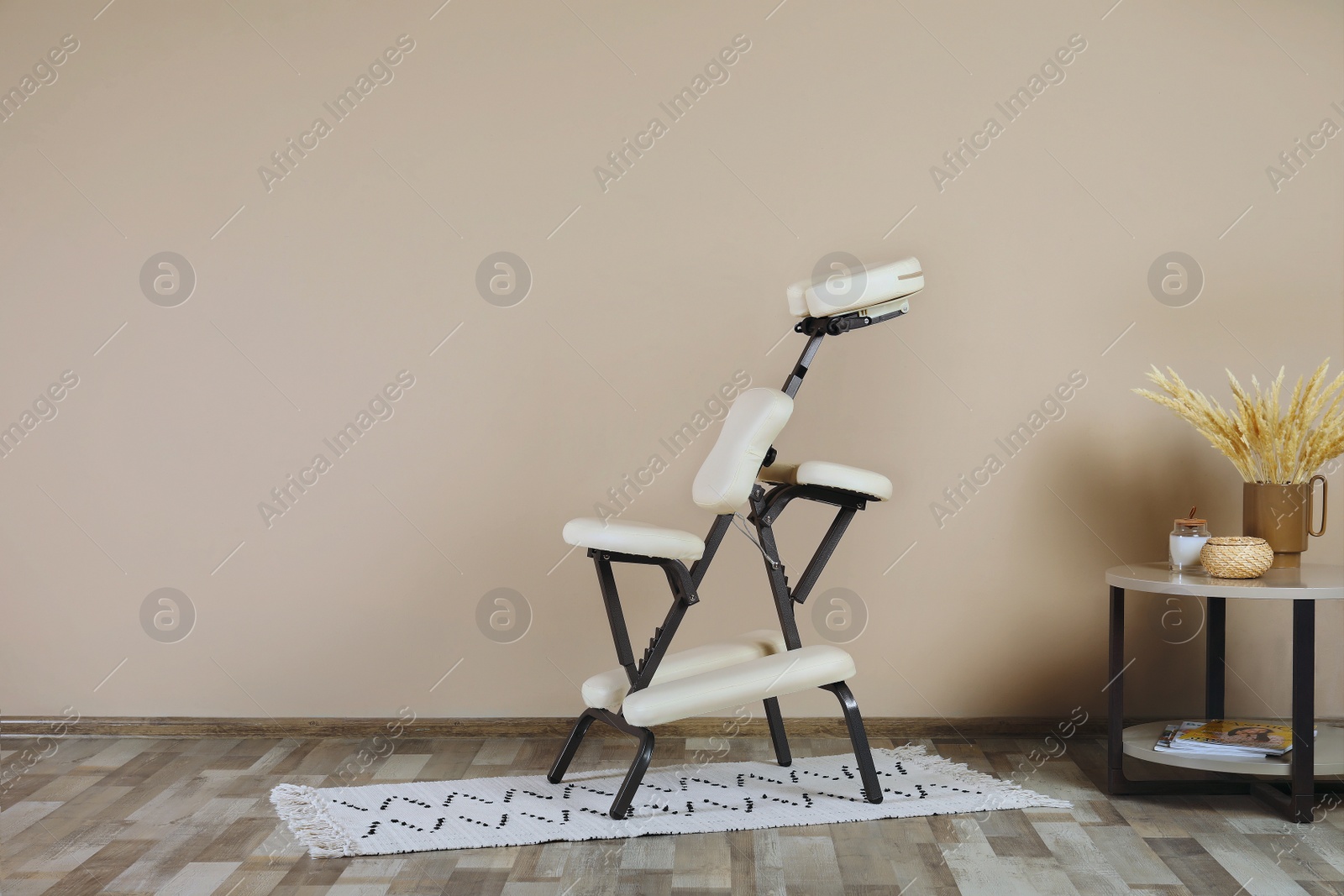 Photo of Modern massage chair and table with decorative elements near beige wall indoors, space for text. Medical equipment