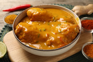 Photo of Tasty chicken curry and ingredients on wooden table, closeup