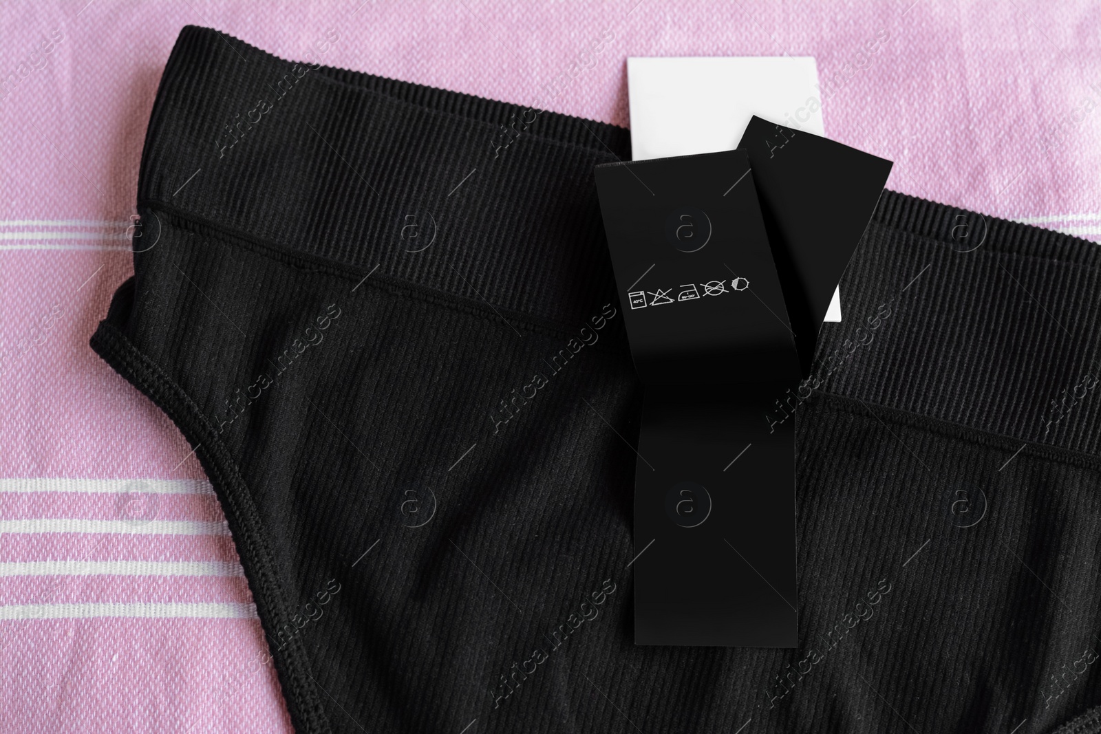 Photo of Clothing label with care information on black garment, top view. Space for text