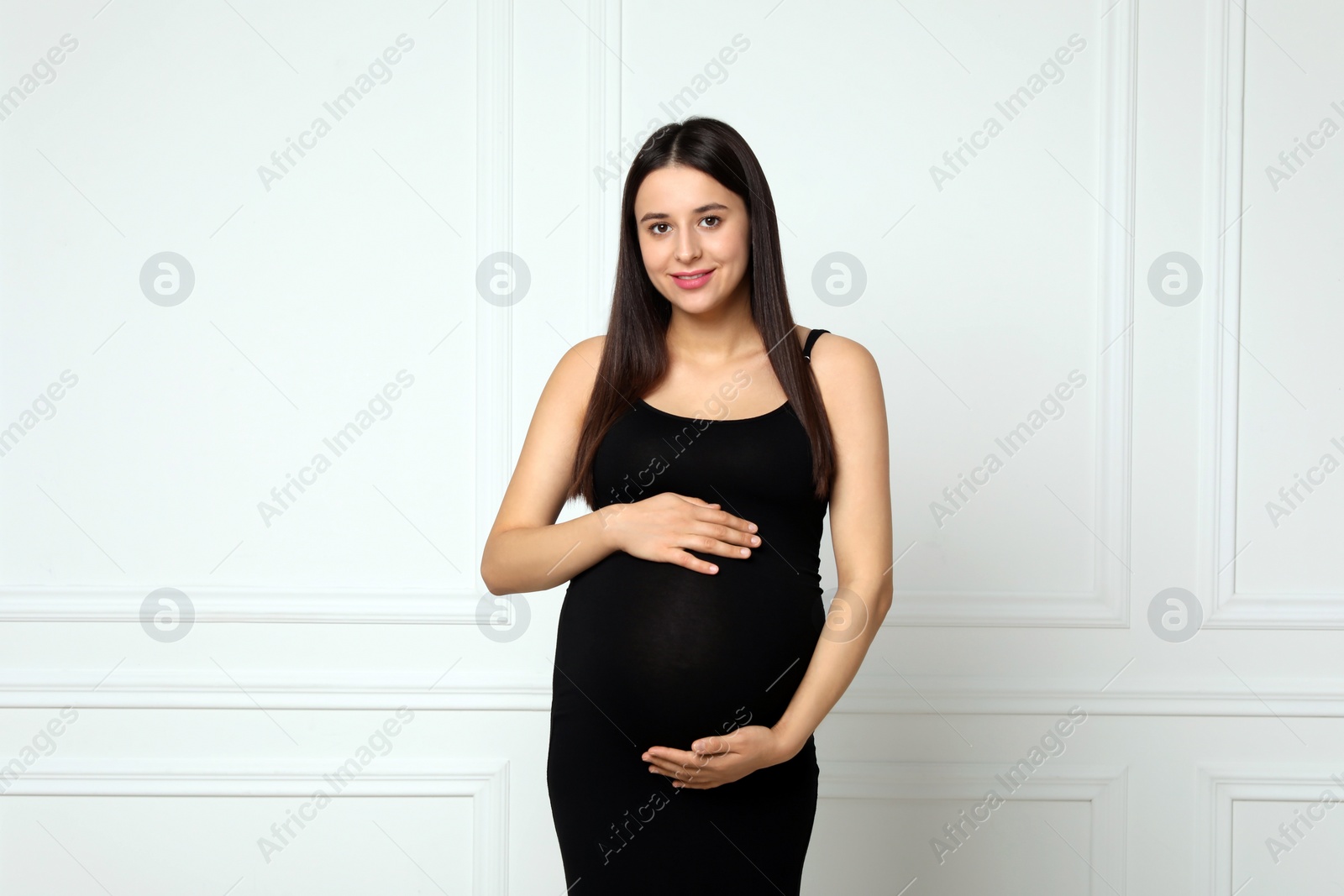 Photo of Beautiful pregnant woman in black dress near light grey wall