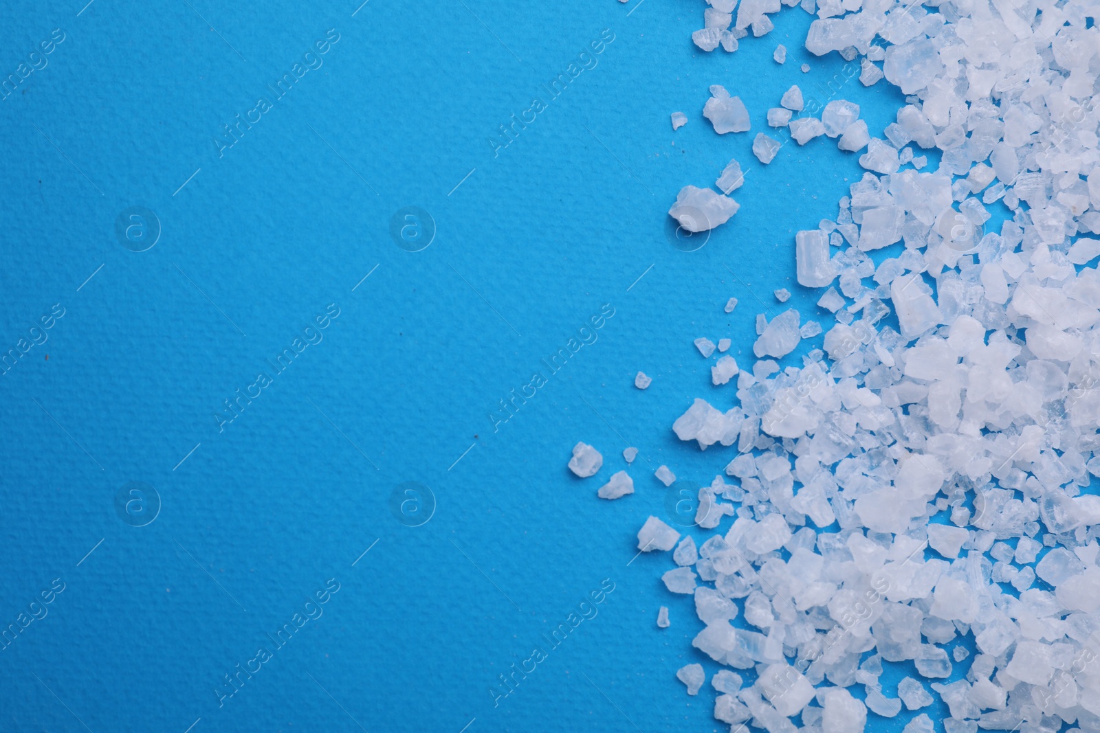 Photo of Sea salt on light blue background, top view. Space for text