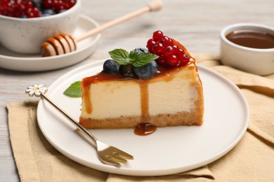 Slice of delicious cheesecake served with berries and caramel sauce on white wooden table, closeup
