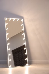 Photo of Stylish mirror with light bulbs near white wall indoors. Interior element