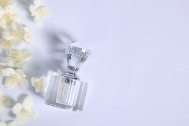 Aromatic perfume in bottle and beautiful jasmine flowers on white background, flat lay. Space for text