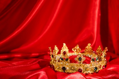 Photo of Beautiful golden crown on red fabric, space for text. Fantasy item