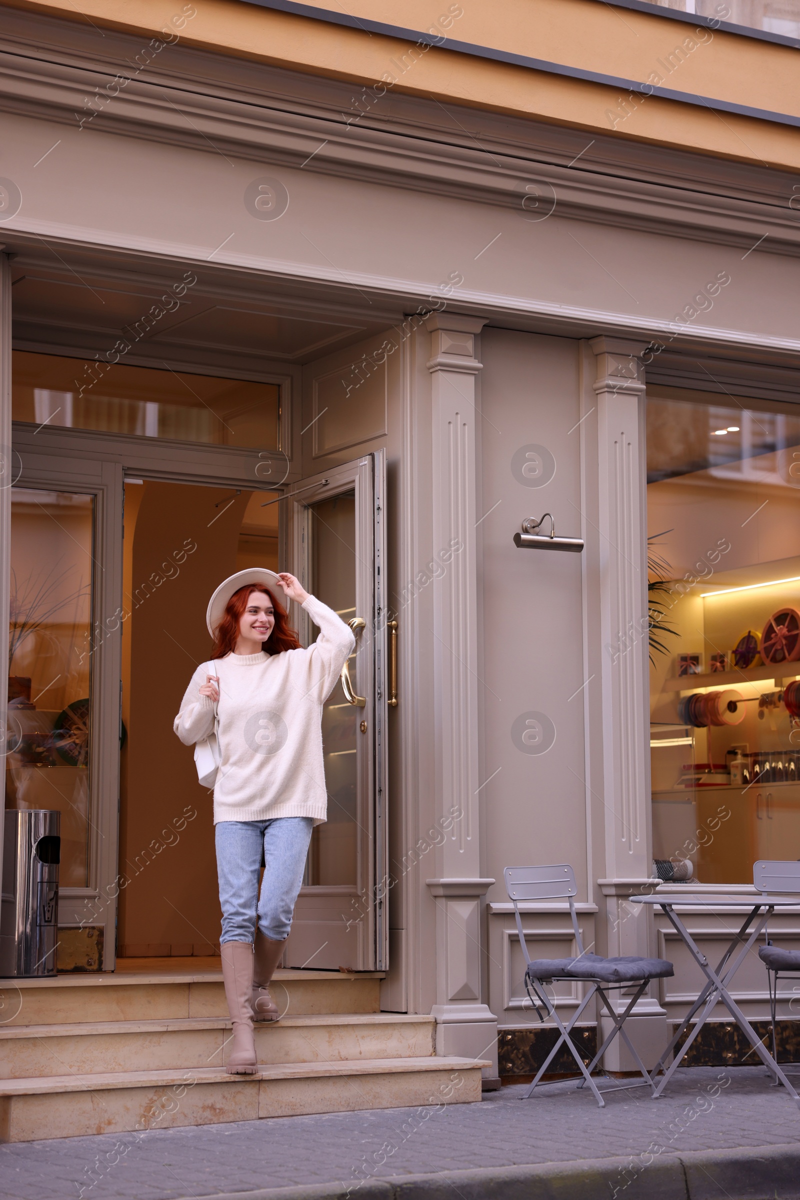 Photo of Smiling woman in hat going out from cafe