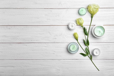 Photo of Jars with body cream and flowers on wooden background