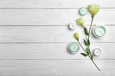 Jars with body cream and flowers on wooden background