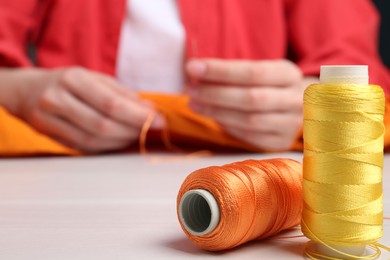 Photo of Woman sewing cloth with needle at light wooden table, focus on spools of threads