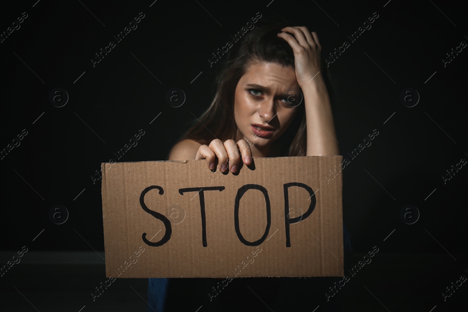 Photo of Crying young woman with sign STOP on black background. Domestic violence concept