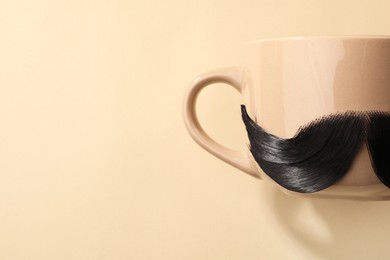 Artificial moustache and cup on beige background, top view. Space for text