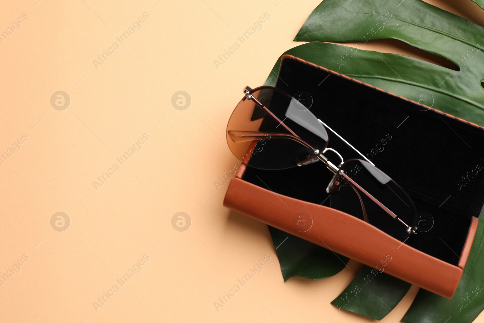Photo of Stylish sunglasses in brown leather case on beige background, top view. Space for text