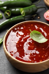 Spicy chili sauce with basil in bowl on black table, closeup