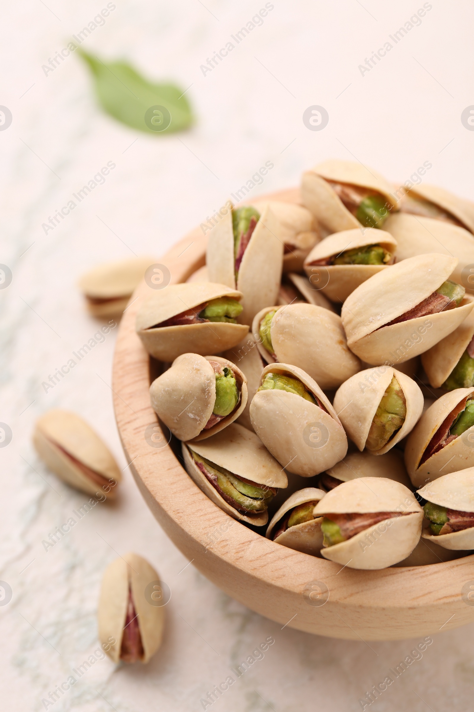 Photo of Delicious pistachios in bowl on white textured table