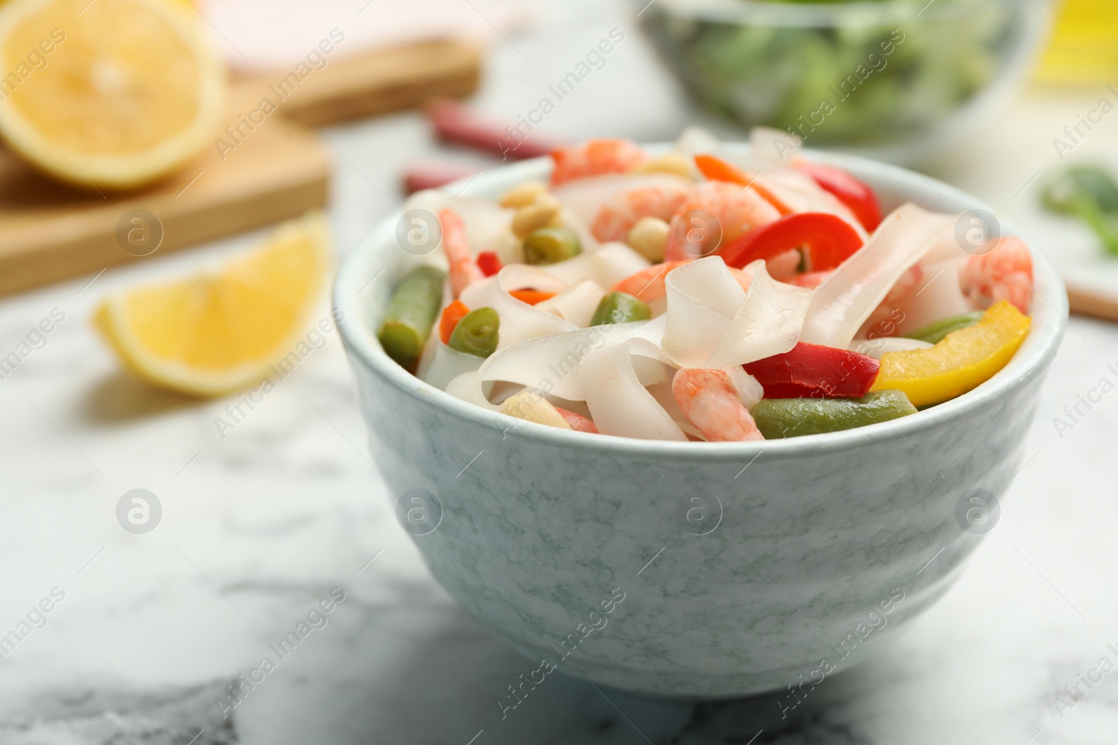 Photo of Tasty cooked rice noodles with shrimps and vegetables on white marble table