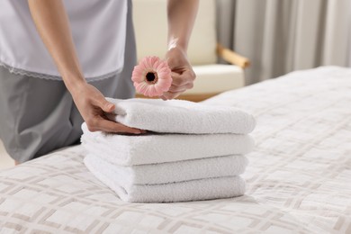 Photo of Chambermaid putting flower on fresh towels in hotel bedroom, closeup