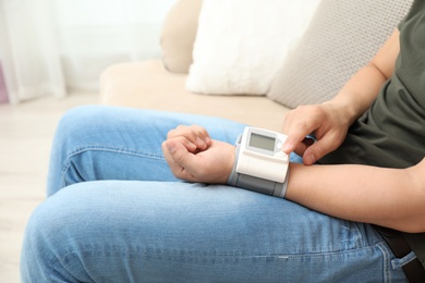 Photo of Young man checking pulse with blood pressure monitor on wrist indoors, closeup