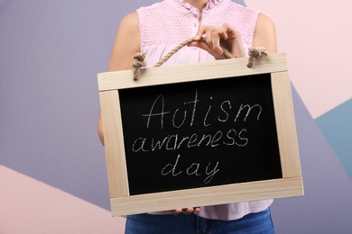 Photo of Woman holding blackboard with phrase "Autism awareness day" on color background