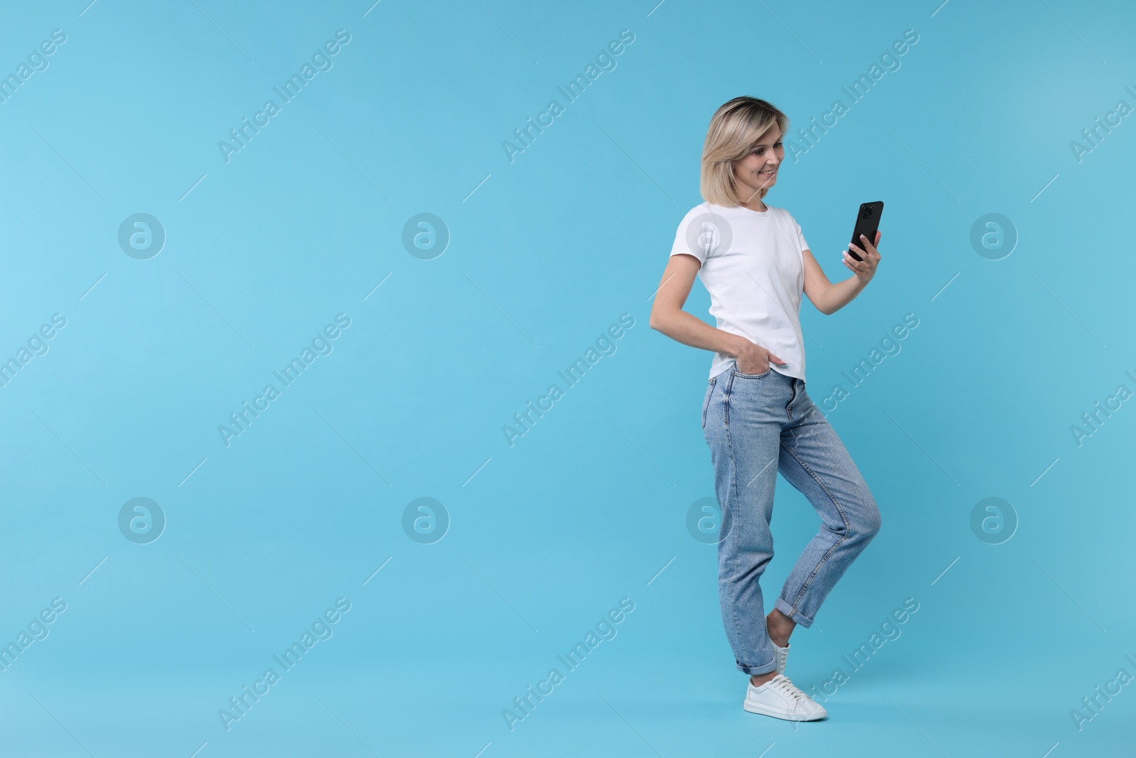 Photo of Happy woman with phone on light blue background, space for text