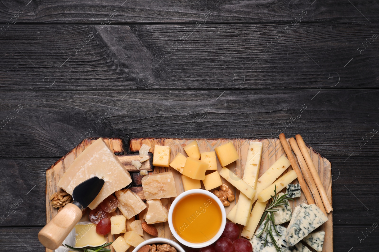 Photo of Cheese plate with honey, grapes and nuts on black wooden table, top view. Space for text