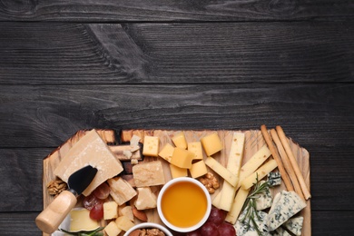 Photo of Cheese plate with honey, grapes and nuts on black wooden table, top view. Space for text