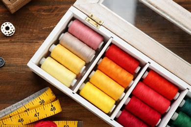 Photo of Container with set of color sewing threads on wooden background