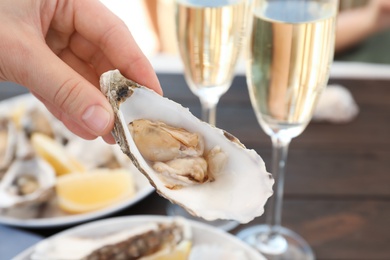 Photo of Woman with fresh oyster over table, focus on hand